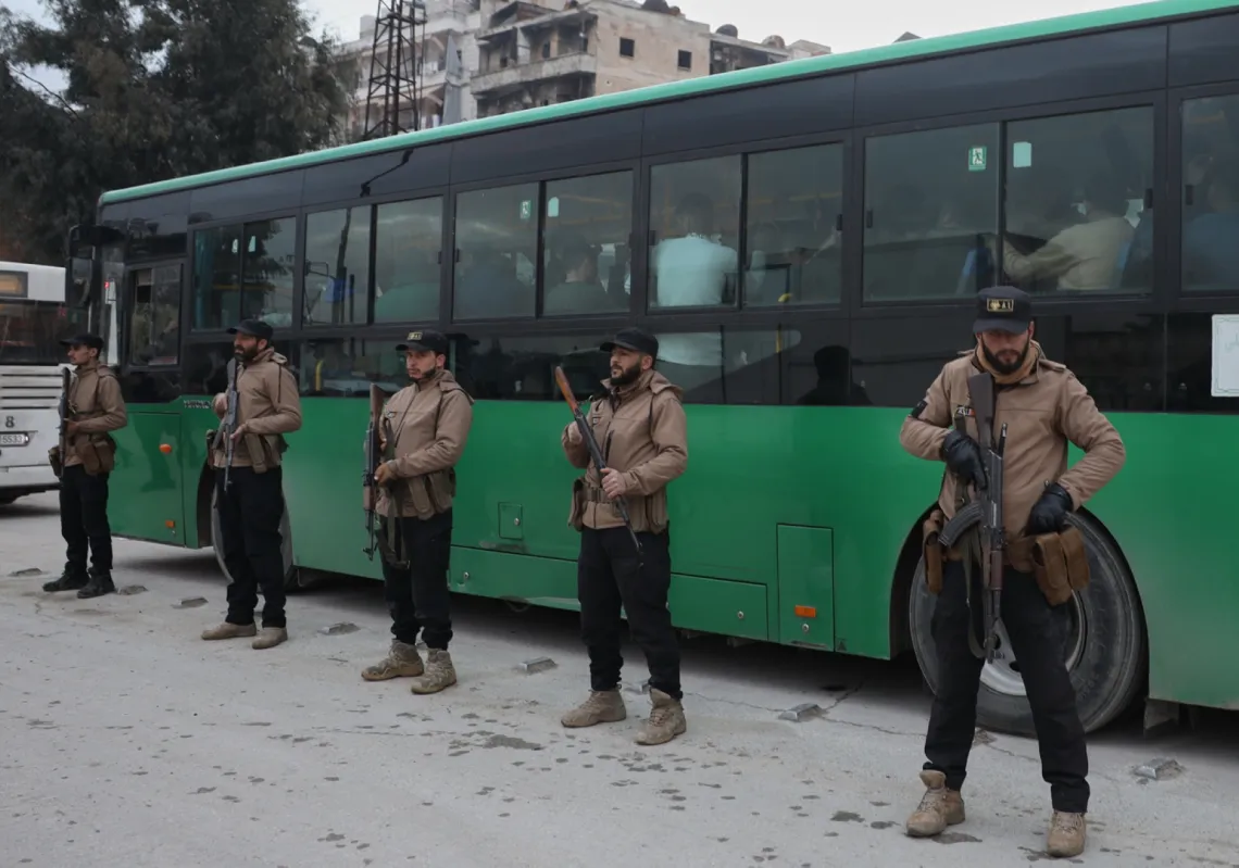 
أفراد من الأمن السوري يقفون بجوار حافلات تقل مقاتلين استسلموا خلال اشتباكات بين القوات الحكومية وقوات سوريا الديمقراطية بقيادة الأكراد في مدينة حلب شمال سوريا، السبت 10 يناير 2026.