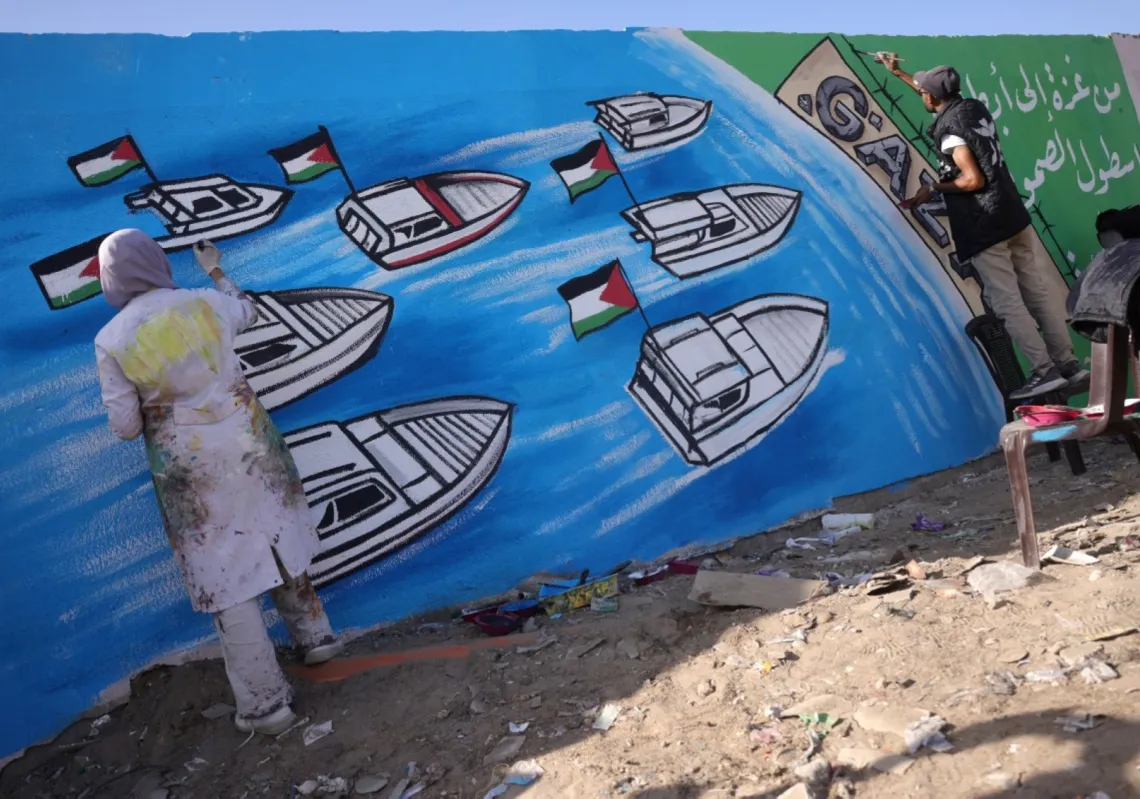 فنانون فلسطينيون يرسمون لوحة جدارية تمثل "أسطول الصمود العالمي" في دير البلح بقطاع غزة، 3 أكتوبر 2025