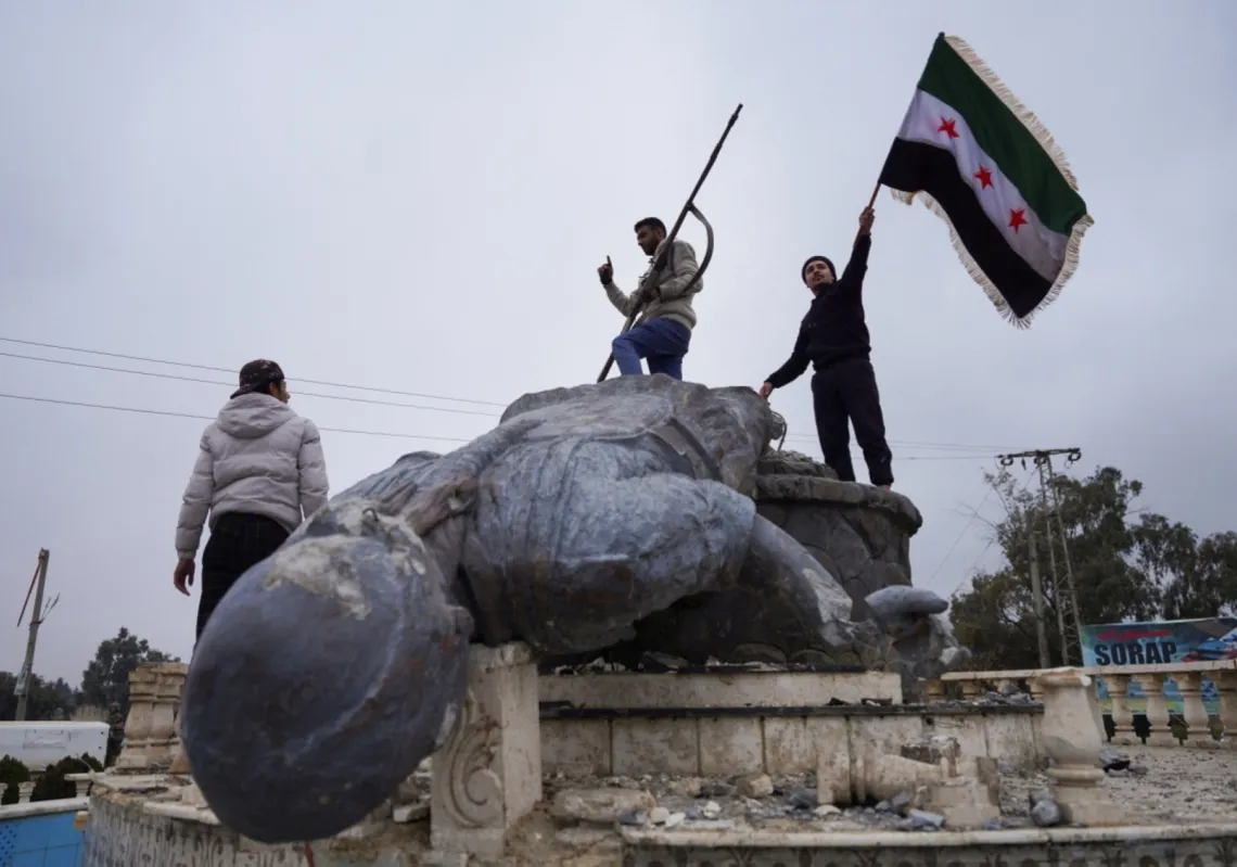 يرفعون العلم السوري فوق تمثال محطم لمقاتلة من "قوات سوريا الديمقراطية" (قسد) في الطبقة شمال شرقي سوريا في 18 يناير/ كانون الثاني 2026