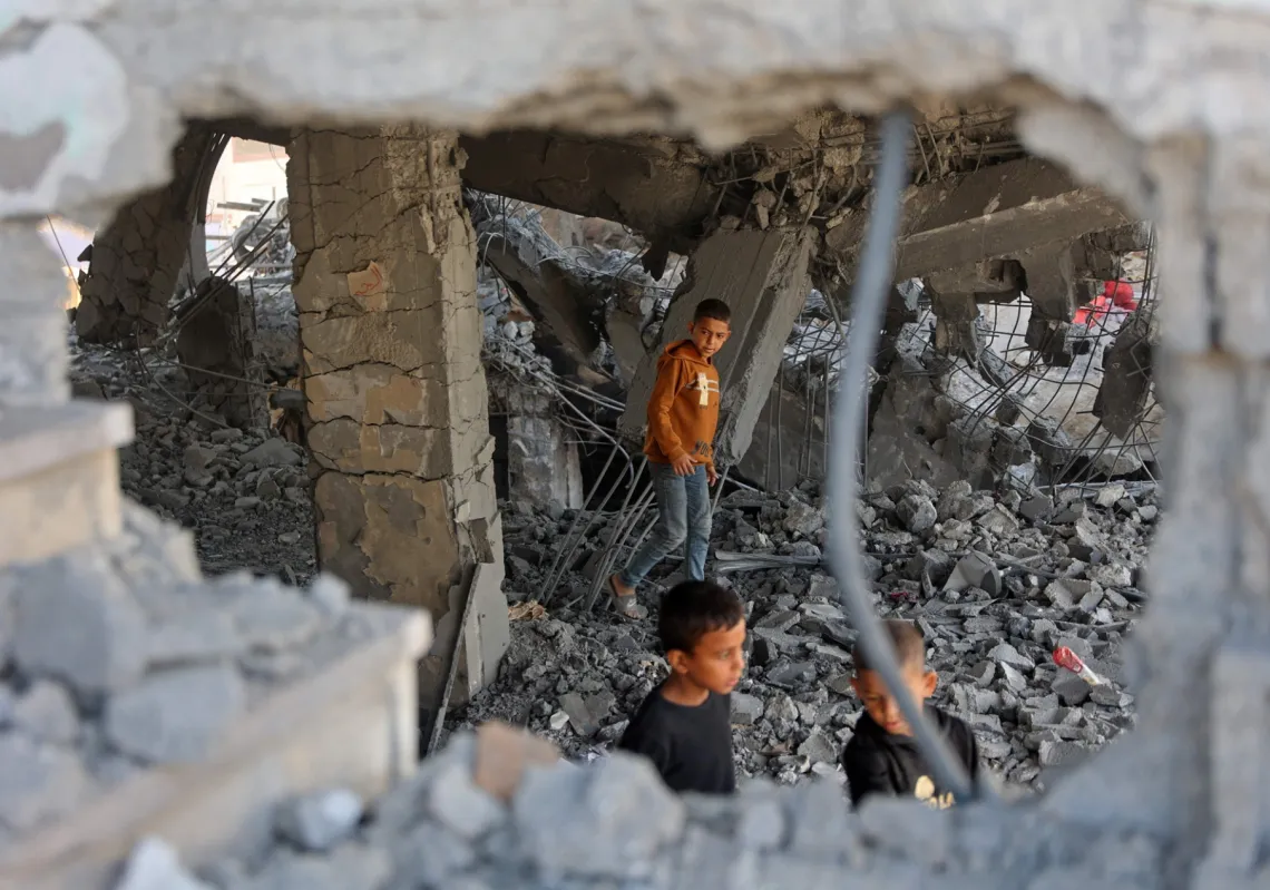 
أطفال فلسطينيون يسيرون وسط أنقاض مبنى متضرر تابع لوزارة الأوقاف، كان يؤوي نازحين في حي الزيتون بمدينة غزة في 20 نوفمبر