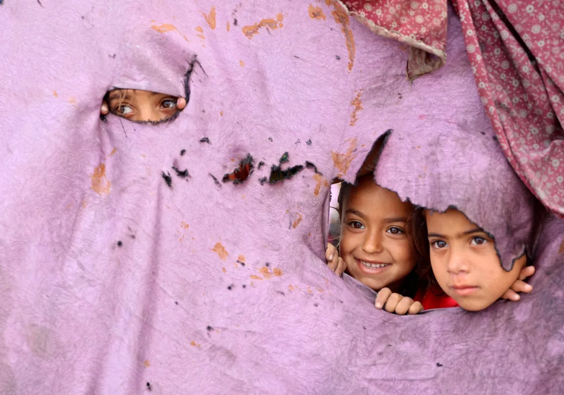 Palestinian children peek out of holes in their tent at a makeshift displacement camp set up amid building rubble in Gaza City on 12 May 2025.