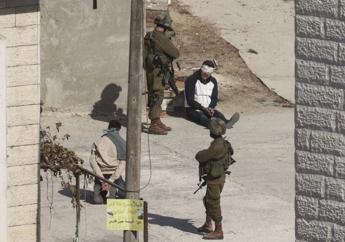 جنود إسرائيليون يقيّدون معتقلا فلسطينيا خلال دهم في دورا جنوب الخليل، 31 أكتوبر 2024