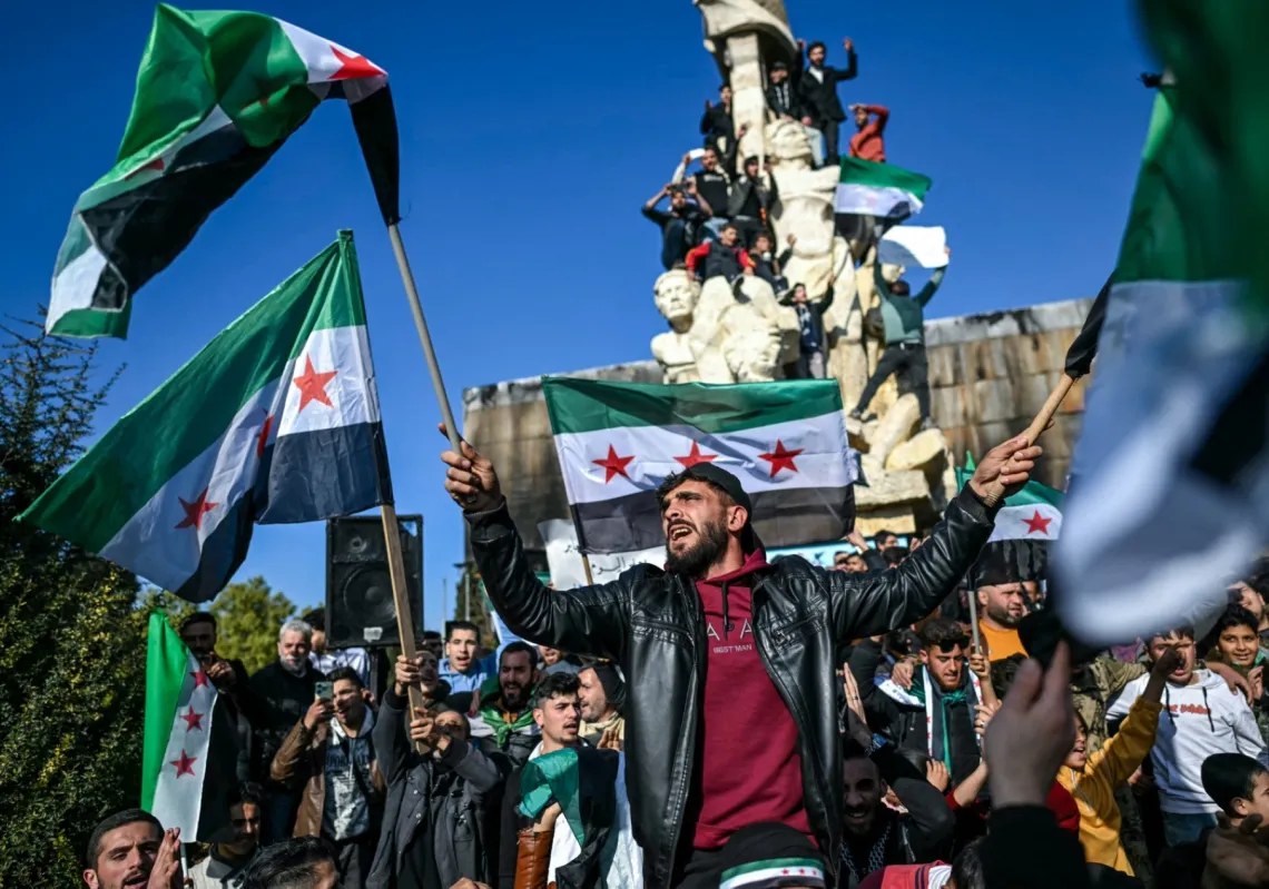 People wave independence-era Syrian flags as they gather at Saadallah al-Jabiri Square after the Friday noon prayer in Aleppo on 13 December 2024.