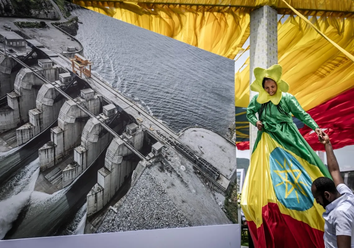 A performer stands next to a decorative aerial image of the Grand Ethiopian Renaissance Dam (GERD) during its official inauguration ceremony in Guba, on 9 September 2025. 