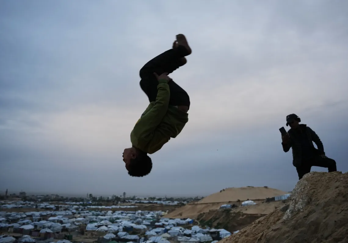 Children practice parkour on a sand dune near tents housing displaced Palestinians in Deir al-Balah, central Gaza Strip, on 1 February 2026. 