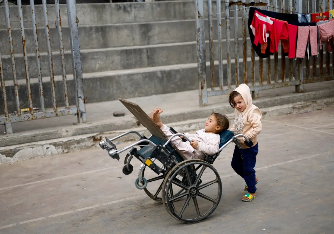 فتاة فلسطينية تدفع رفيقة لها على كرسي متحرك في مخيم يأوي فلسطينيين نزحوا خلال العدوان الإسرائيلي الذي استمر عامين، في مدينة غزة، 9 فبراير