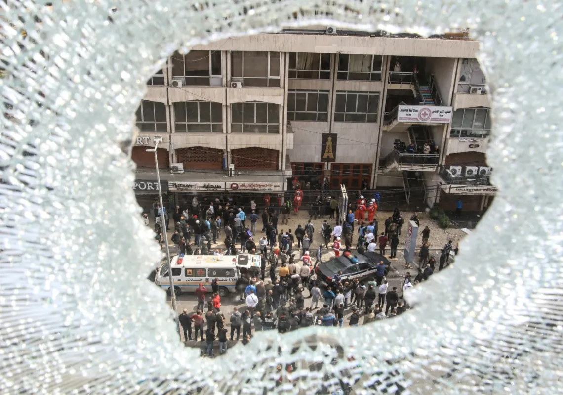 نافذة محطمة تُطل على فرق الإسعافات الأولية والقوى الأمنية العاملة قرب مبنى استُهدف بغارة جوية إسرائيلية في مدينة صيدا الساحلية جنوب لبنان في 6 مارس 2026