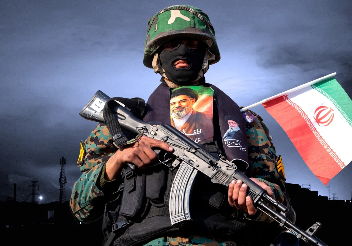 يراقب أحد أفراد قوات الأمن، حاملًا صورة المرشد الأعلى الإيراني الجديد مجتبى خامنئي، المتظاهرين أثناء تجمعهم في مسيرة تأييد للمرشد الأعلى الجديد في ساحة انقلاب بطهران، إيران، في 9 مارس 2026