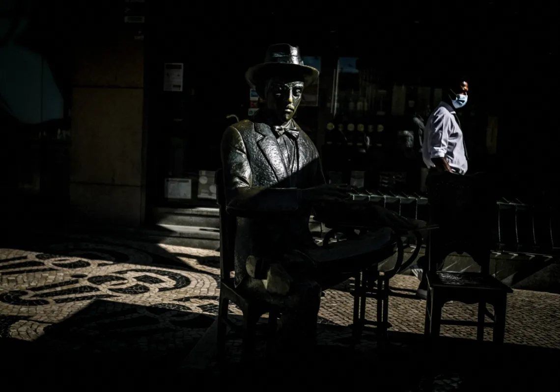 A waiter walks past the statue of Portuguese poet Fernando Pessoa in front of the famous A Brasileira café in Lisbon, on 14 July 2021.