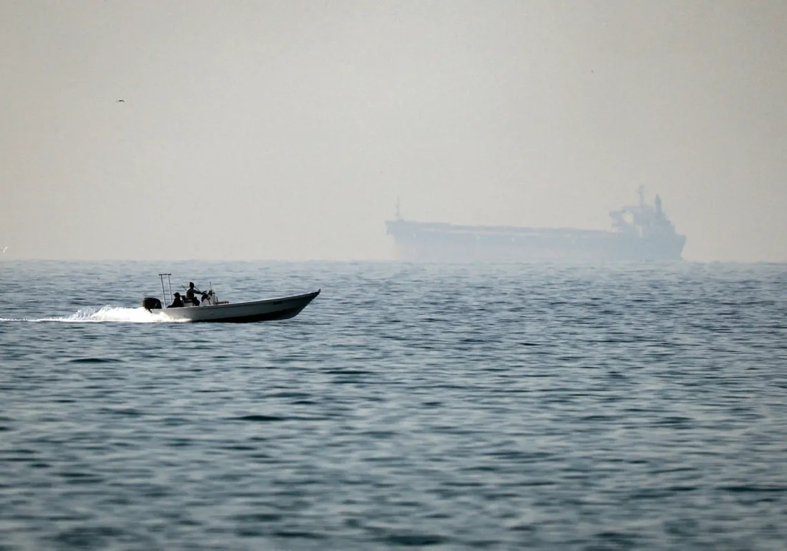 قارب صغير يبحر قبالة بلدة الجير في رأس الخيمة قرب مضيق هرمز، بينما تظهر ناقلة نفط في الخلفية، 25 فبراير 2026