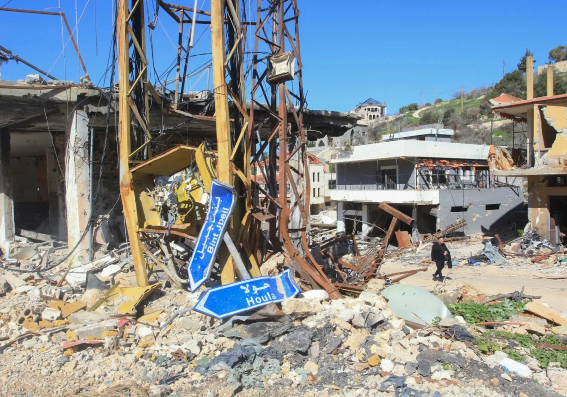 
رجل لبناني يسير وسط الدمار متجاوزاً اللافتات التي تشير إلى الطريق المؤدي إلى قريتي الحولة وبنت جبيل، بينما يتفقد الناس منازلهم المتضررة في قرية العديسة جنوب لبنان في 18 فبراير 2025