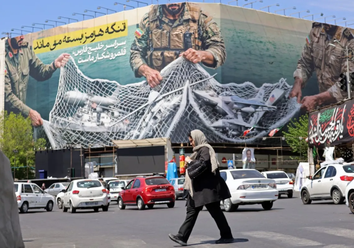 امرأة تمر أمام لوحة ضخمة كتب عليها "مضيق هرمز لا يزال مغلقا" في ساحة الثورة بطهران، 12 أبريل 2026