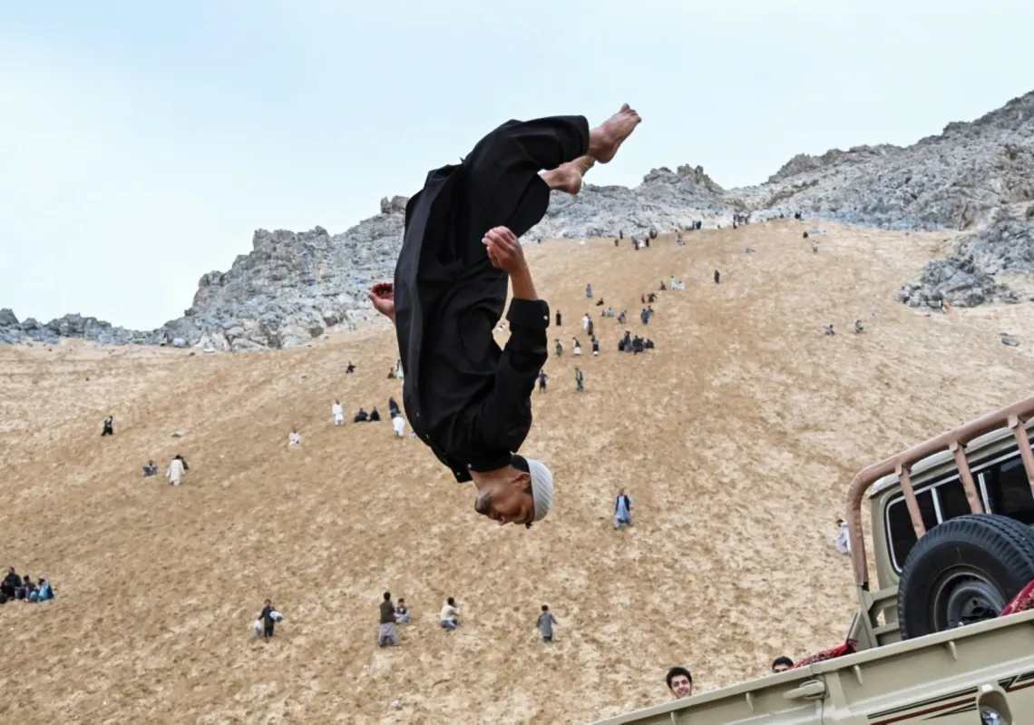 An Afghan parkour athlete performs a stunt on the back of a vehicle on a weekend in the sandy mountainside at the Sayad area of Reg-e-Rawan in Kapisa province on 24 April 2026.