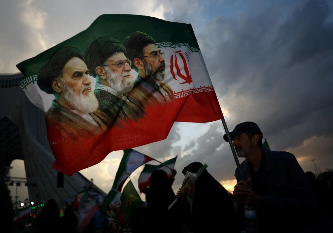 A man holds a flag featuring the late leader of the Islamic Revolution Ayatollah Ruhollah Khomeini, the late Supreme Leader of Iran Ali Khamenei and the new leader, Mojtaba Khamenei, at a rally in Tehran on 29 April 2026.