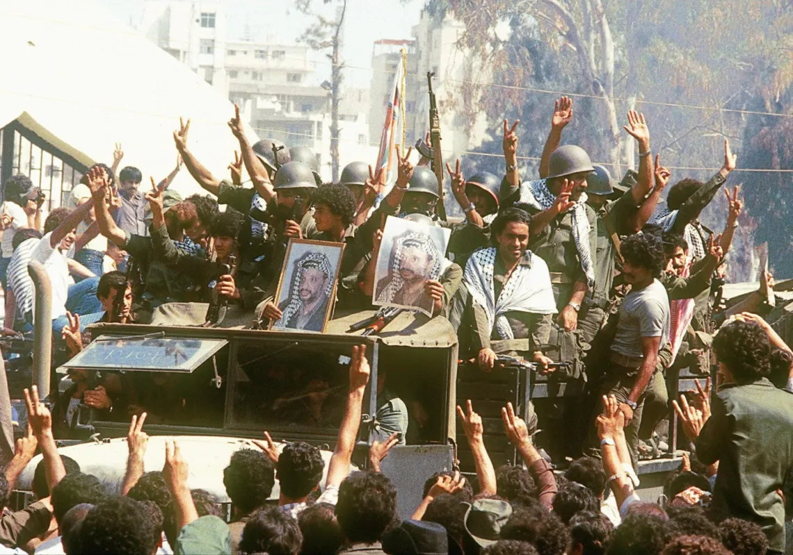 مقاتلون فلسطينيون يظهرون في صورة مؤرخة 22 أغسطس 1982 وهم يرفعون علامات النصر ويحملون صورة زعيمهم ياسر عرفات، في بيروت، أثناء توجههم إلى تونس