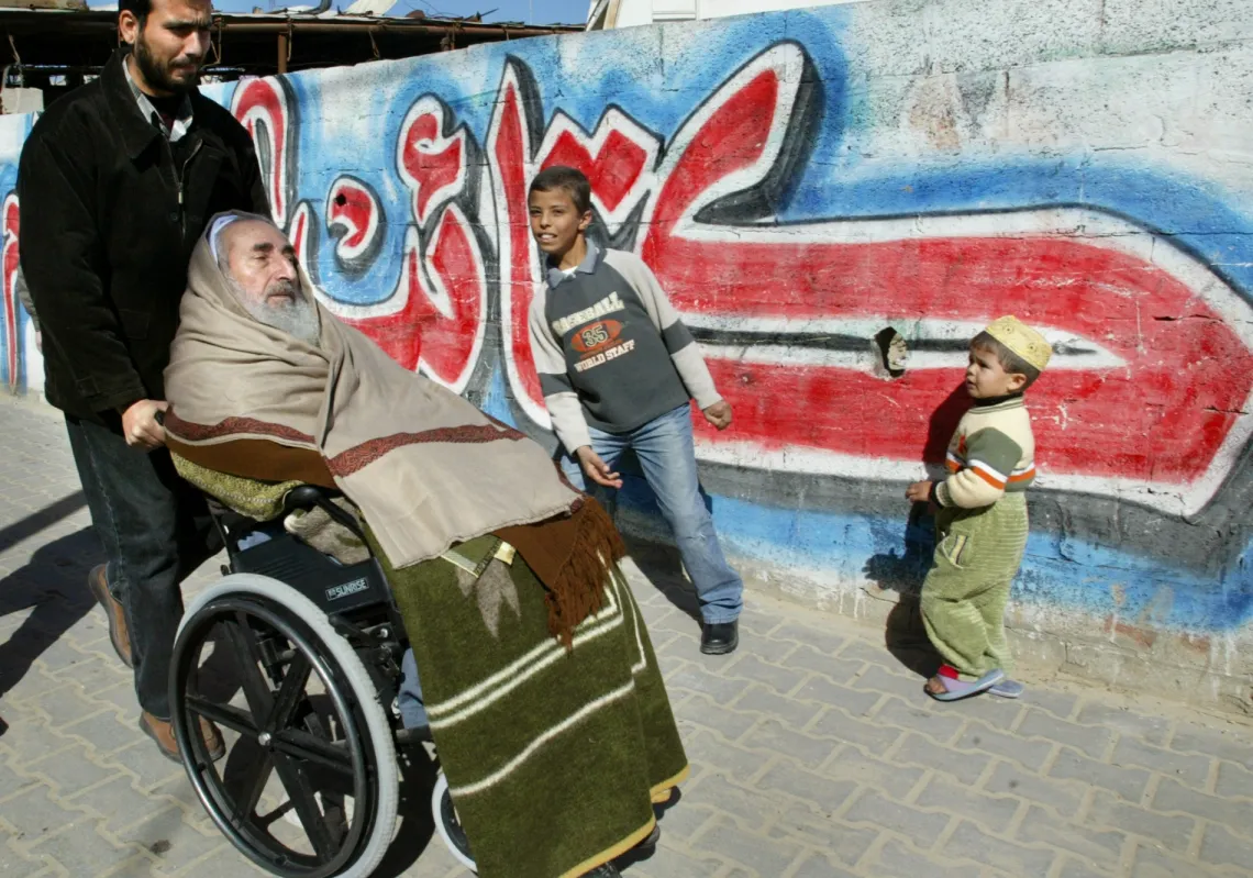 الشيخ أحمد ياسين، الزعيم الروحي لحركة "حماس" على كرسي متحرك في طريقه لأداء صلاة الجمعة في المسجد بمدينة غزة يرافقه حارسه، في 30 يناير 2004