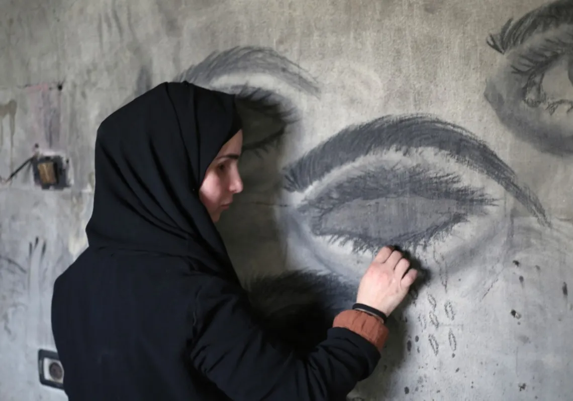 Areej al-Saafin, who lost her eye as a result of an Israeli military strike, uses charcoal to draw on the wall of her home in the Bureij Palestinian refugee camp in the central Gaza Strip on 2 May 2026.