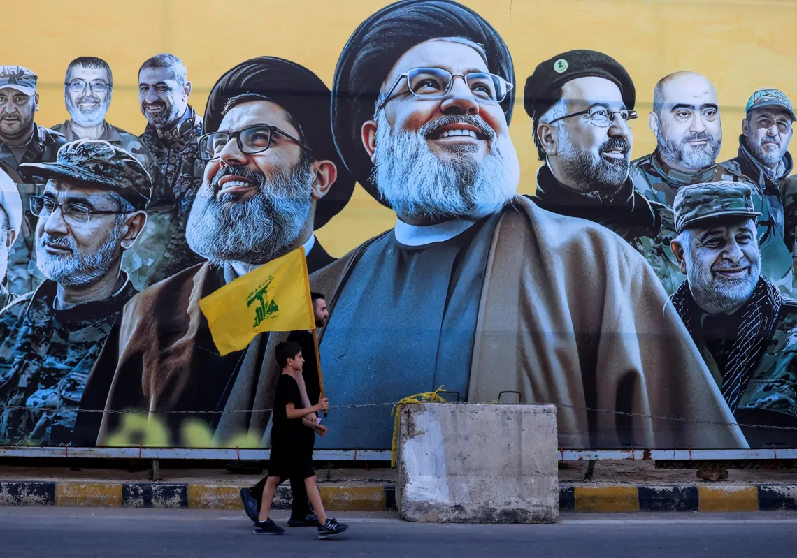 A man walks with a boy past a mural in Beirut depicting former Hezbollah leader Hassan Nasrallah and other senior figures, on the day Hezbollah chief Naim Qassem delivers a televised speech on 17 June 2026.