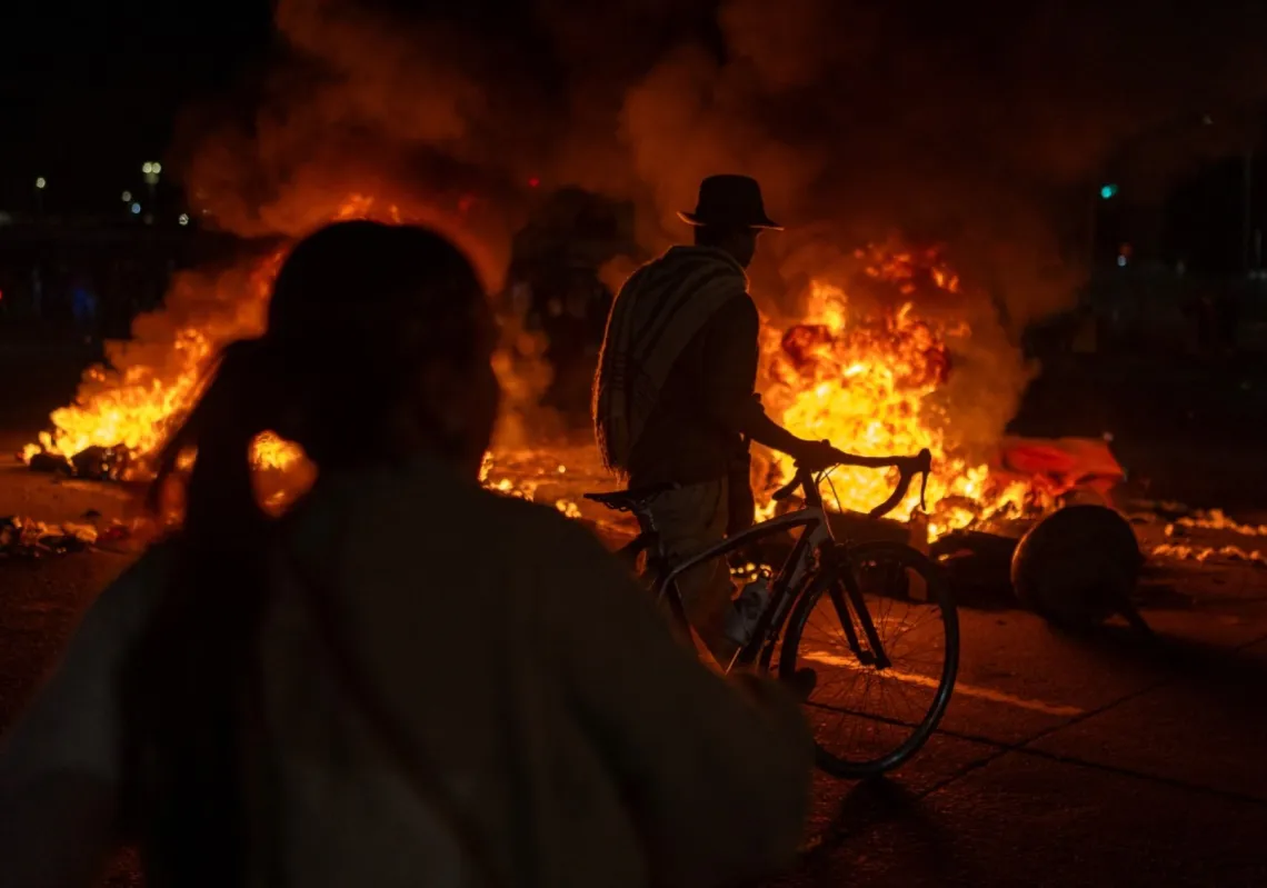 A man walks his bike as demonstrators stand in front of burning barricades during clashes over the preliminary results of the presidential runoff election in Bogota, Colombia, on 21 June 2026.