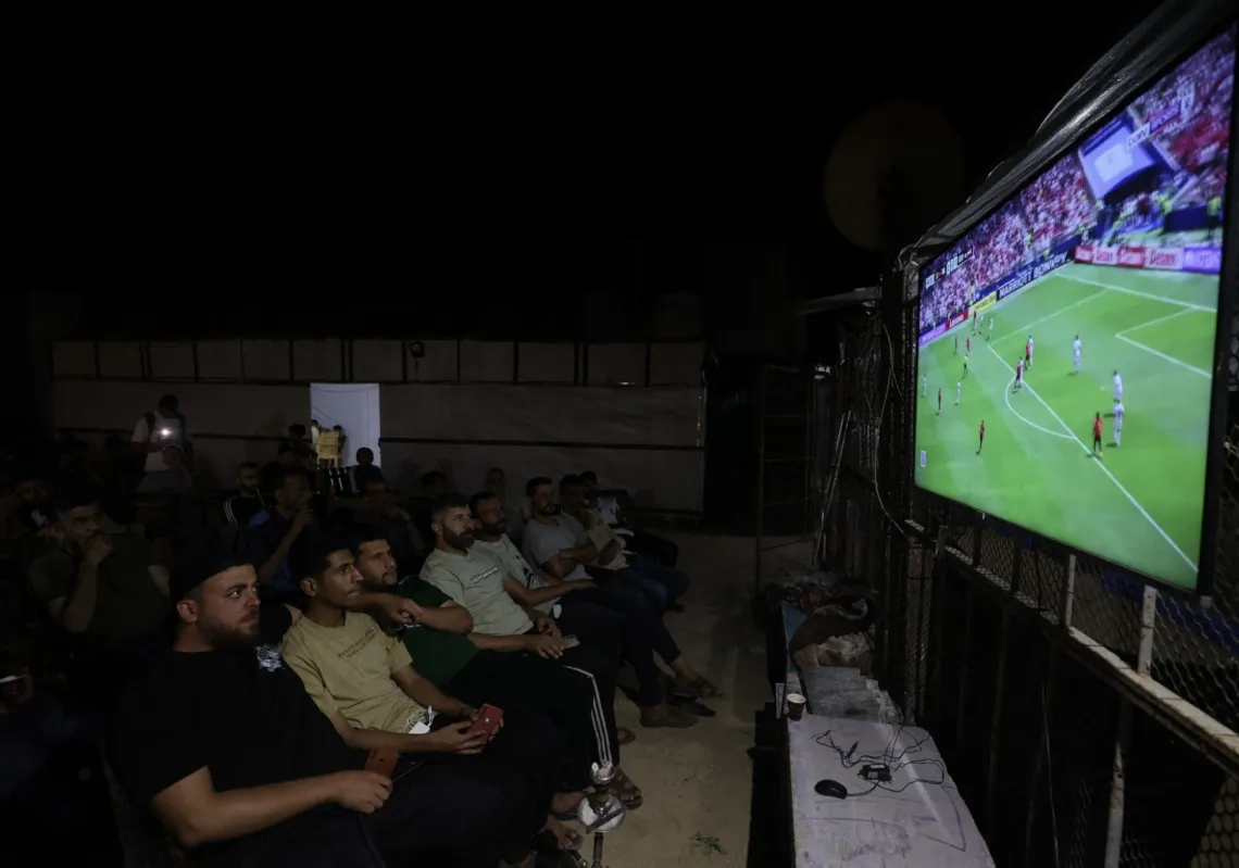 نازحون في قطاع غزة، يشاهدون مباراة بلجيكا ومصر في كأس العالم على شاشة عملاقة نُصبت في مخيم النصيرات للاجئين وسط قطاع غزة، في 15 يونيو