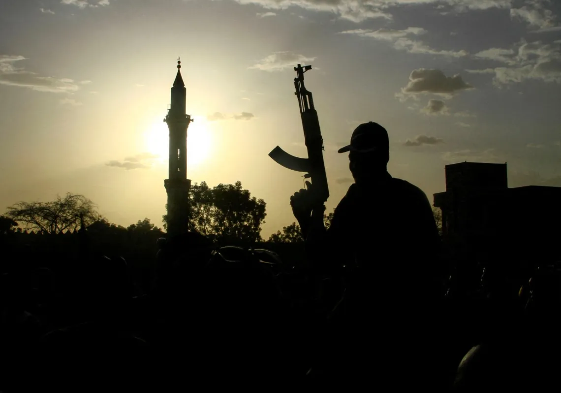 A fighter loyal to Sudan's army chief Abdel Fattah al-Burhan holds up a weapon backdropped by the minaret of a mosque, during a graduation ceremony in the southeastern Gedaref state on 27 May 2024.