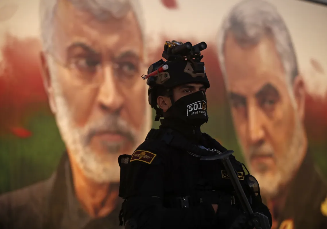 A member of Iraq's PMF stands in front of a banner depicting slain Iraqi commander Abu Mahdi al-Muhandis (L) and Iranian commander Qassem Soleimani, on January 2, 2023.