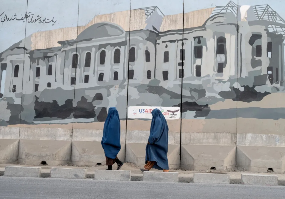 نساء أفغانيات يرتدين البُرقُع يمررن أمام جدارية على جانب الطريق في كابل في 11 ديسمبر 2025
