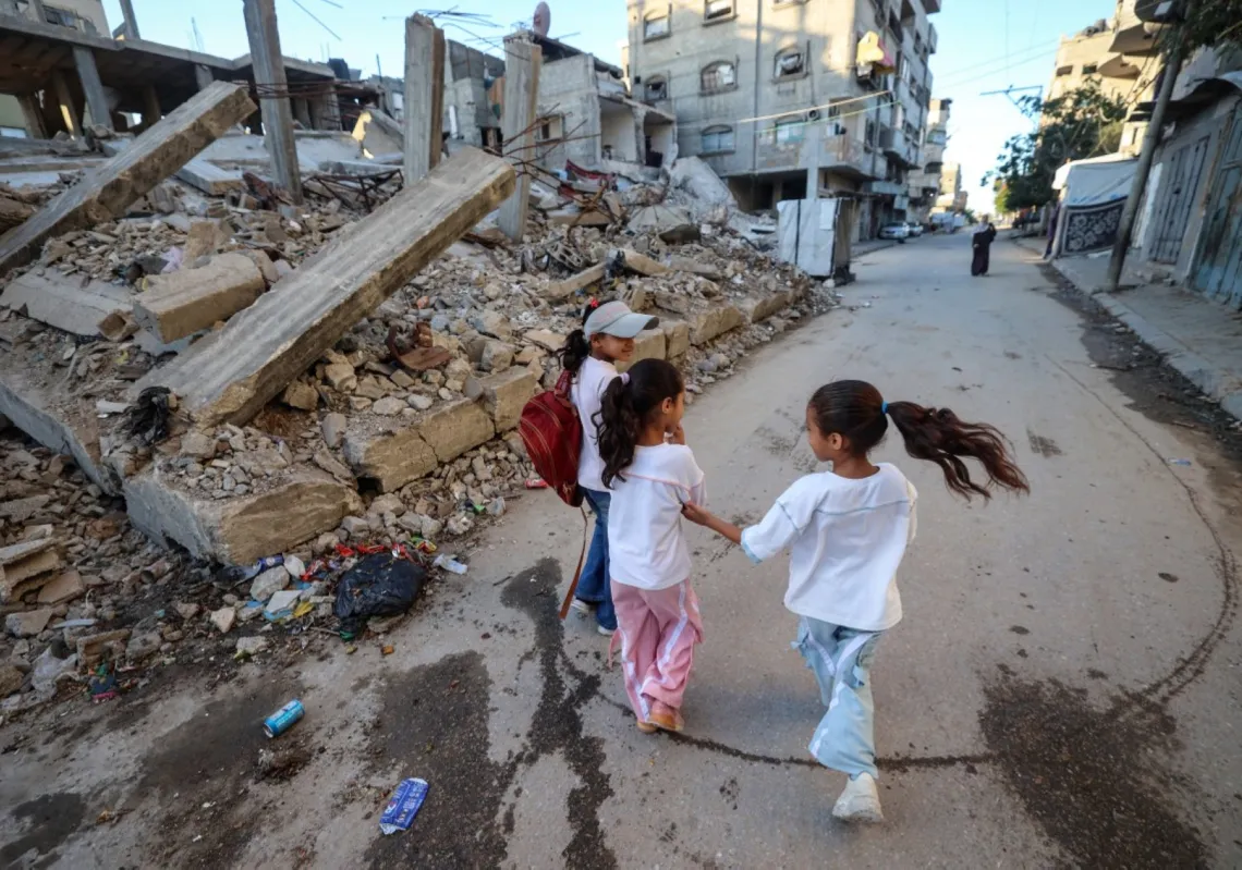 أطفال فلسطينيون يسيرون إلى المدرسة مرورا بأنقاض مبنى مدمر مع بدء العام الدراسي في مخيم البريج وسط قطاع غزة، في 19 سبتمبر 