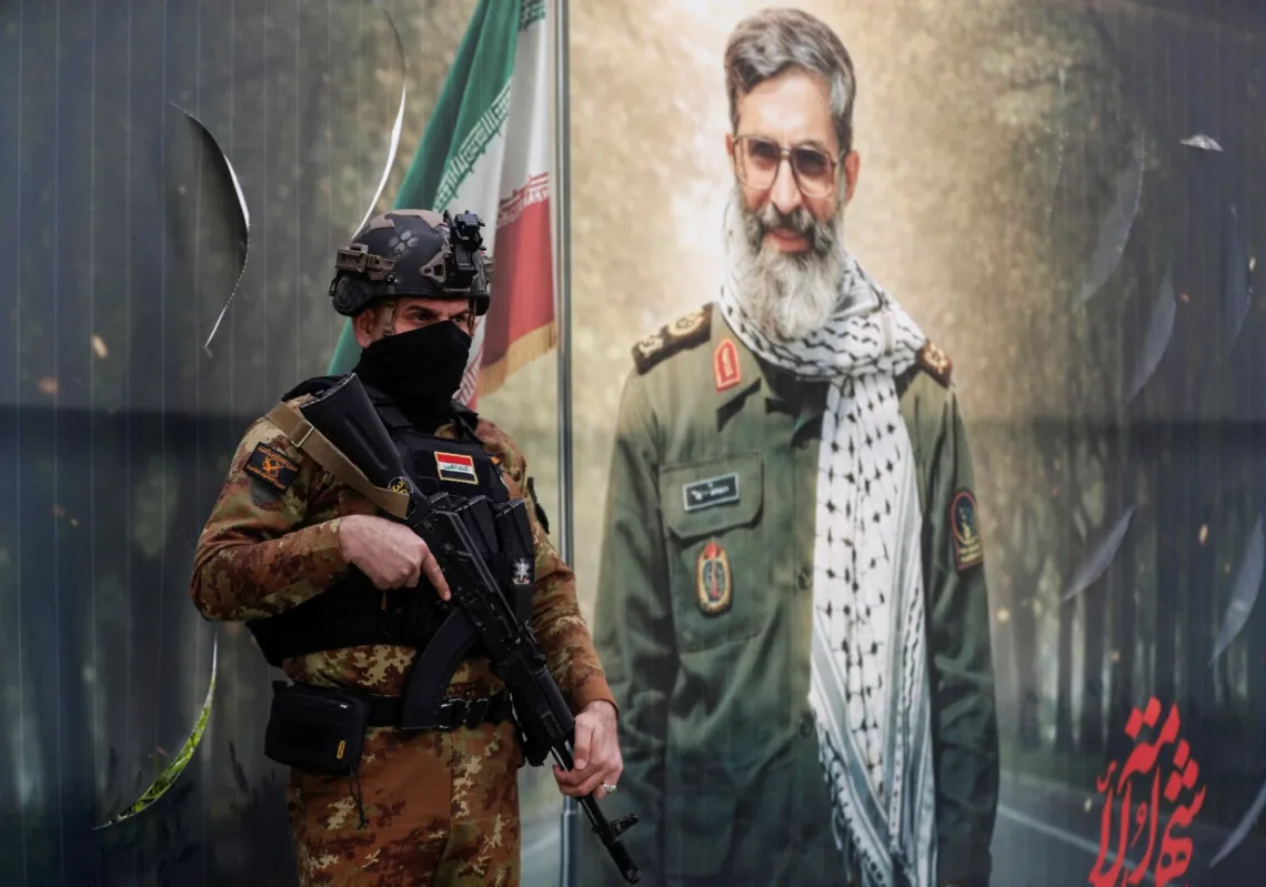 A member of Iraq's Hashed al-Shaabi Forces stands in front of a banner depicting a younger Ayatollah Ali Khamenei, Iran’s slain supreme leader, in Baghdad's Tahrir Square on 12 March 2026.