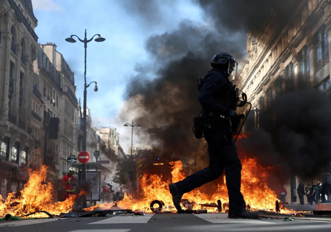 French riot police walk past burning objects in a street amid clashes with protesters in Paris as part of nationwide protests against the cost of living and rising fuel prices on 17 October 2026. 