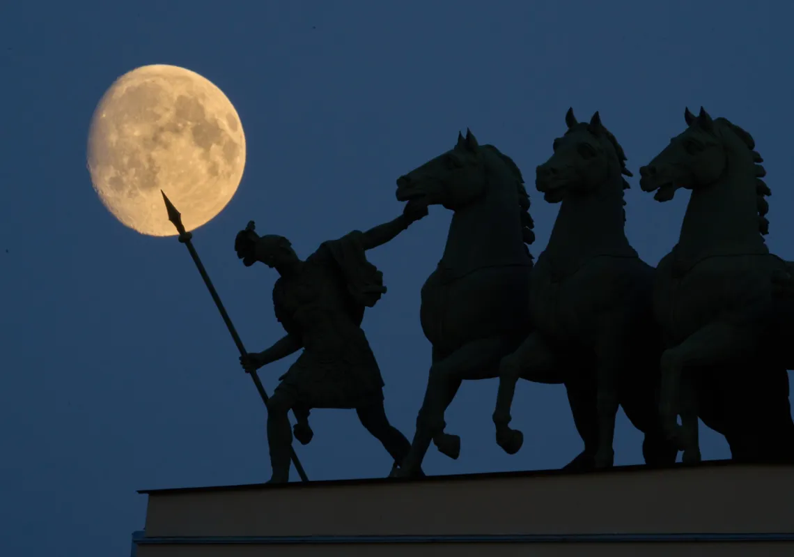 The moon rises over a chariot statue atop the General Staff Headquarters in St. Petersburg, Russia, on 23 October 2026. 
